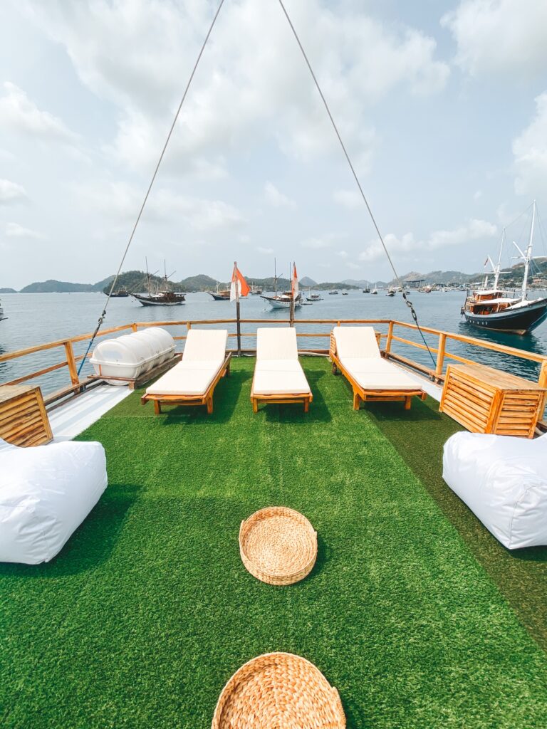 Green turf sundeck with white loungers, bean bags and other boats anchored beyond
