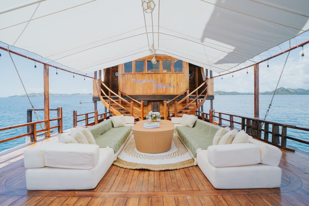 Shaded deck lounge with white sofas, a woven rattan table and framed signage behind
