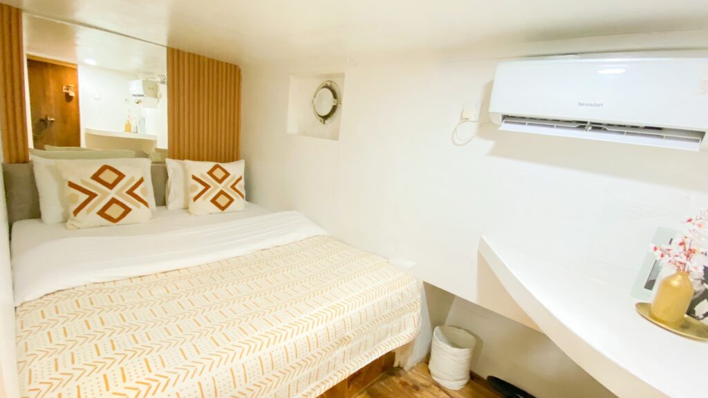 Deluxe cabin bed with patterned pillows, a porthole window and wall-mounted air conditioning