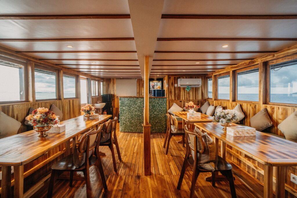 Indoor dining area with long wooden tables, floral arrangements and wide sea-view windows