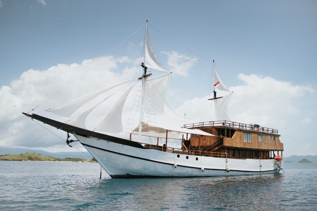 Zada Nara Komodo liveaboard phinisi under full sail against a mountainous coastline