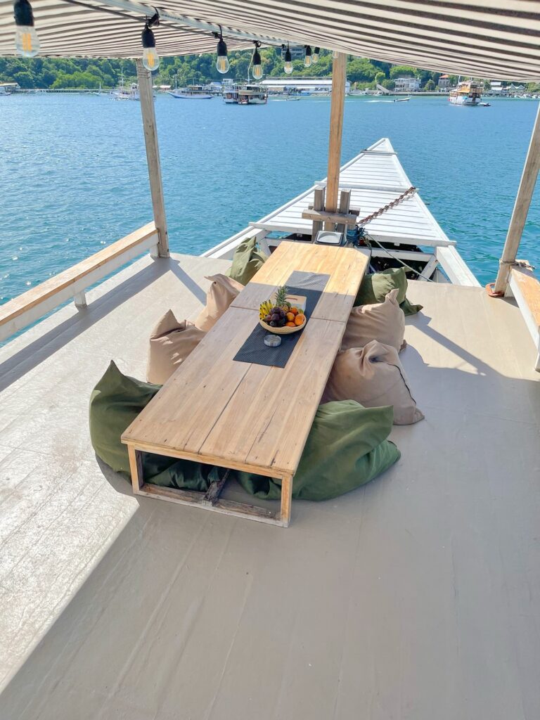 Wooden dining table with a fruit bowl on the bow deck, olive bean bags under a striped canopy