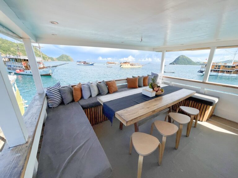 Shaded deck lounge on Zendaya with cushioned bench seating, a wooden table, and stools overlooking a busy harbor