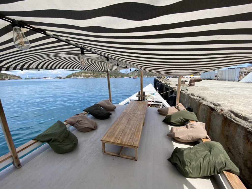 Open-air dining table under a striped canopy on Zendaya, flanked by olive bean bags with ocean views