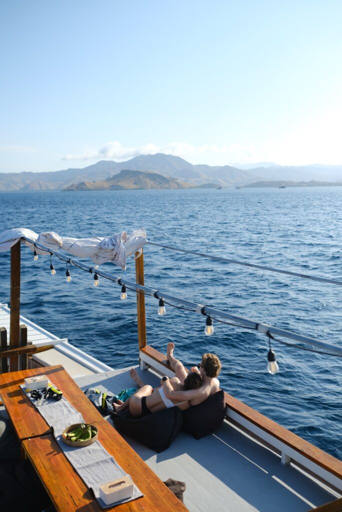 A guest relaxing on bean bags at the bow, looking out over calm water toward distant hills
