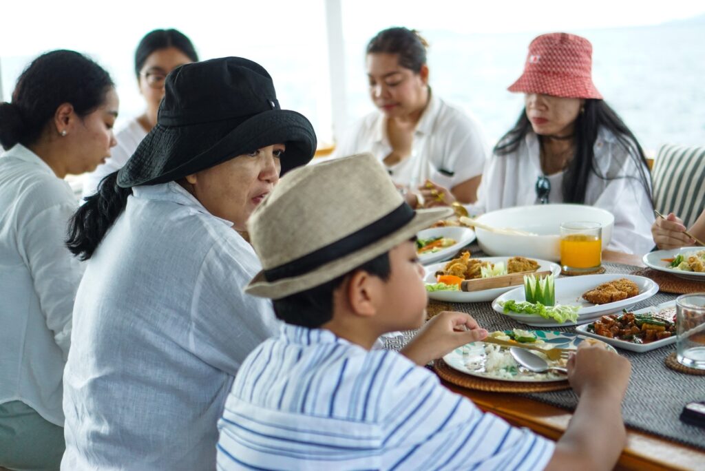 Group of guests wearing sun hats sharing a meal together at a shaded dining table