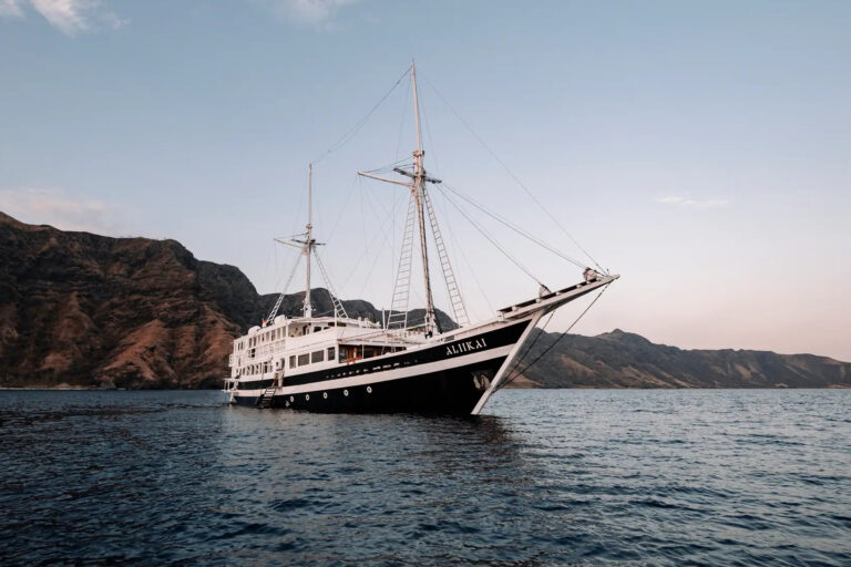 Aliikai voyage underway with sails raised past steep dry hills