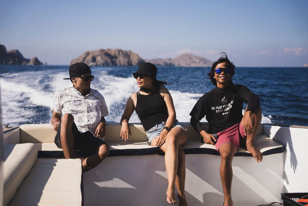 Three people sitting on a speedboat rear seating, wake and rocky islands behind