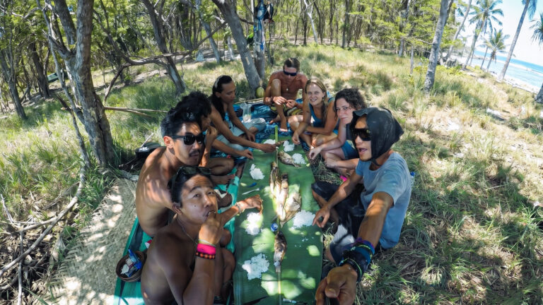 Crew and friends share a picnic lunch on banana leaves under trees by the beach