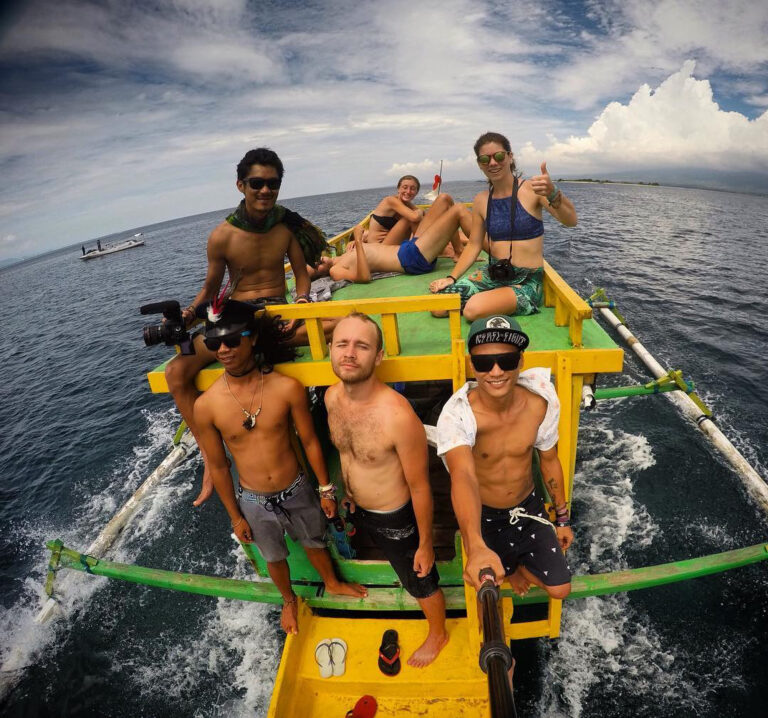 Crew and travelers pose on the bow of a yellow outrigger on open water