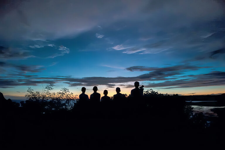 Five figures silhouetted on a hilltop against a blue and orange dusk sky