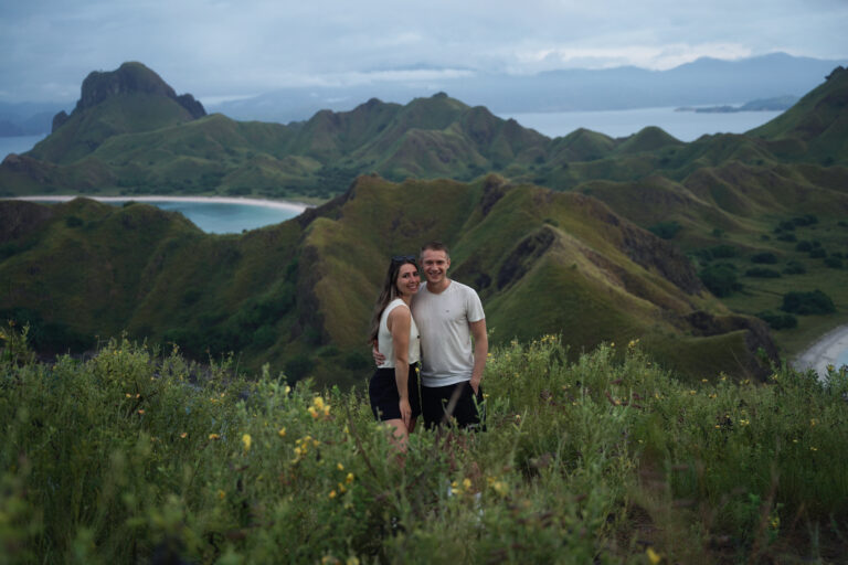Couple standing among wildflowers on green Padar Island hills with the bays behind, Komodo