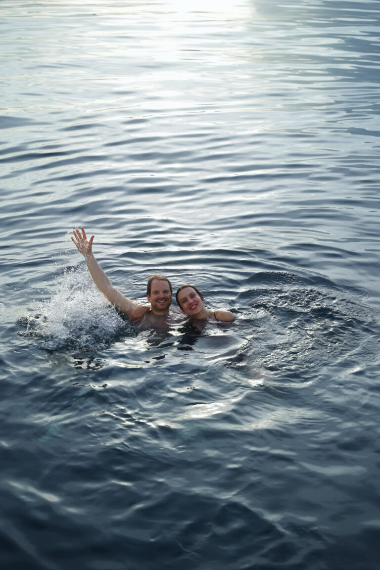 Couple treading water and waving in open sea, seen from the deck above