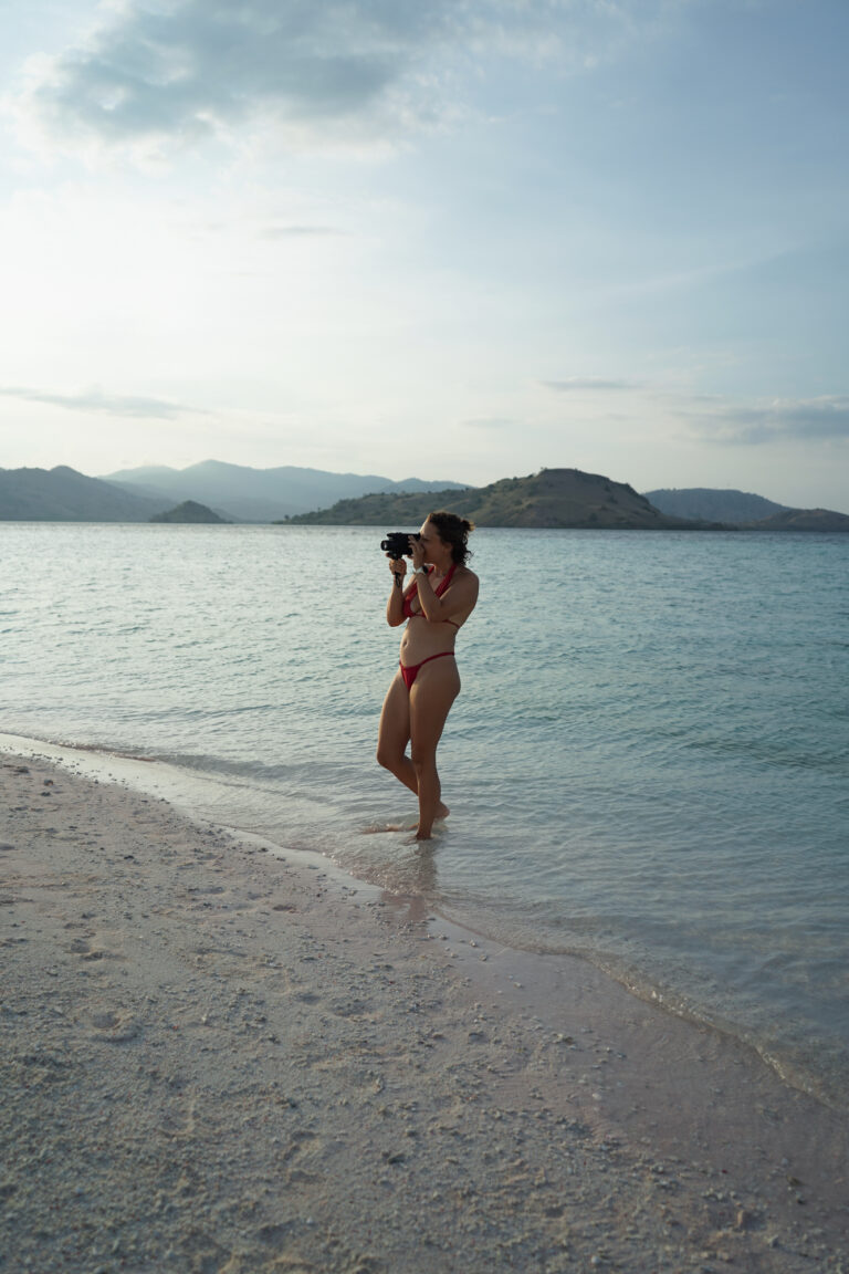 Traveler taking a photo from the shoreline of a white beach, dry islands behind, Komodo