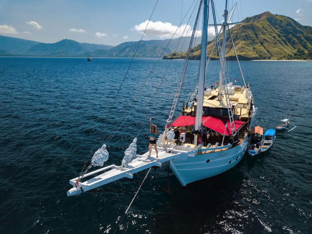 Woman stands on bowsprit netting with red deck canopy behind