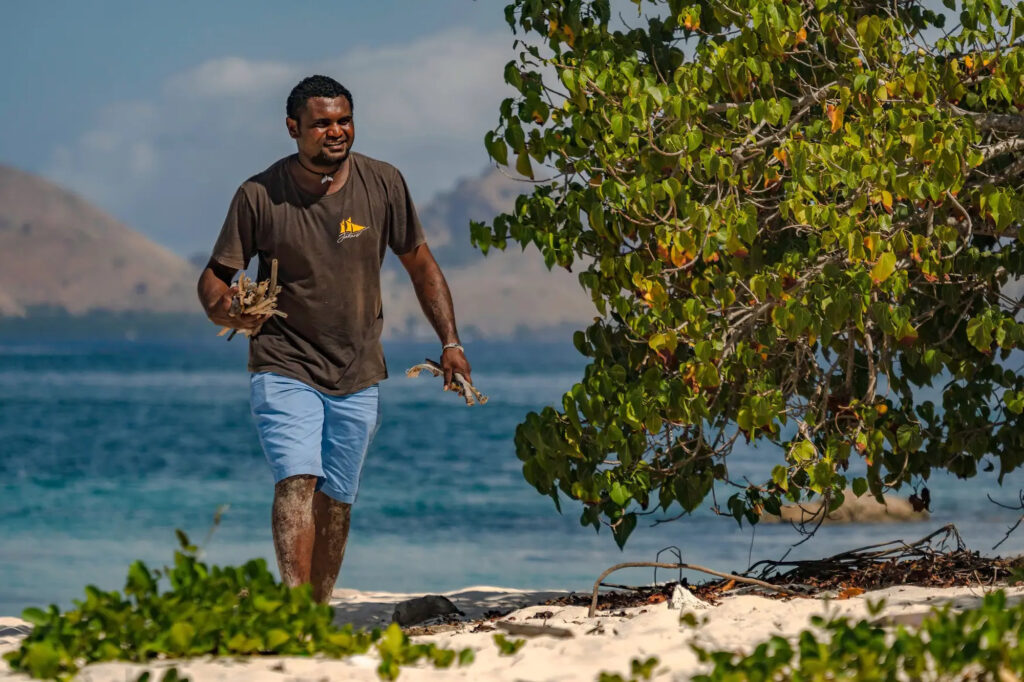 Crew member carries coconut shells along a sandy beach