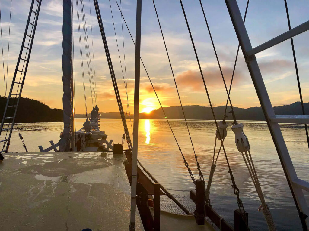 Deck rigging silhouetted against low sun and calm water