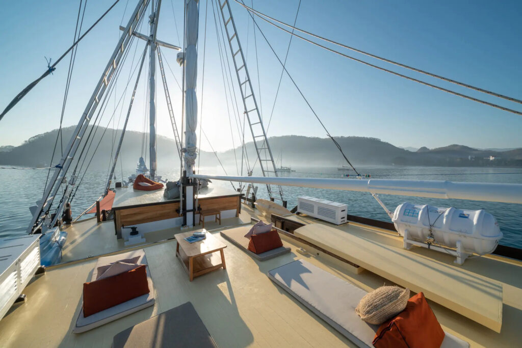 Deck view at sunrise with mast, rigging and cushioned seating