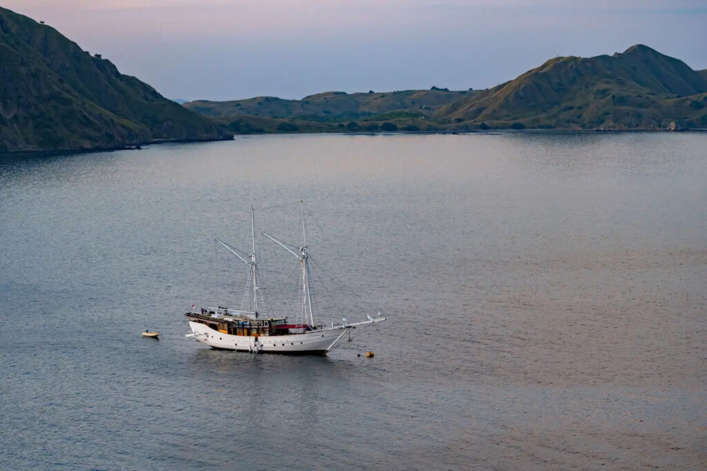 Jakare anchored at dusk in calm water between green hills