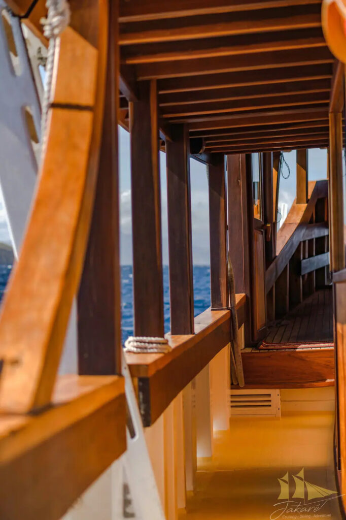 Covered side corridor aboard Jakare with wood beams and ocean view
