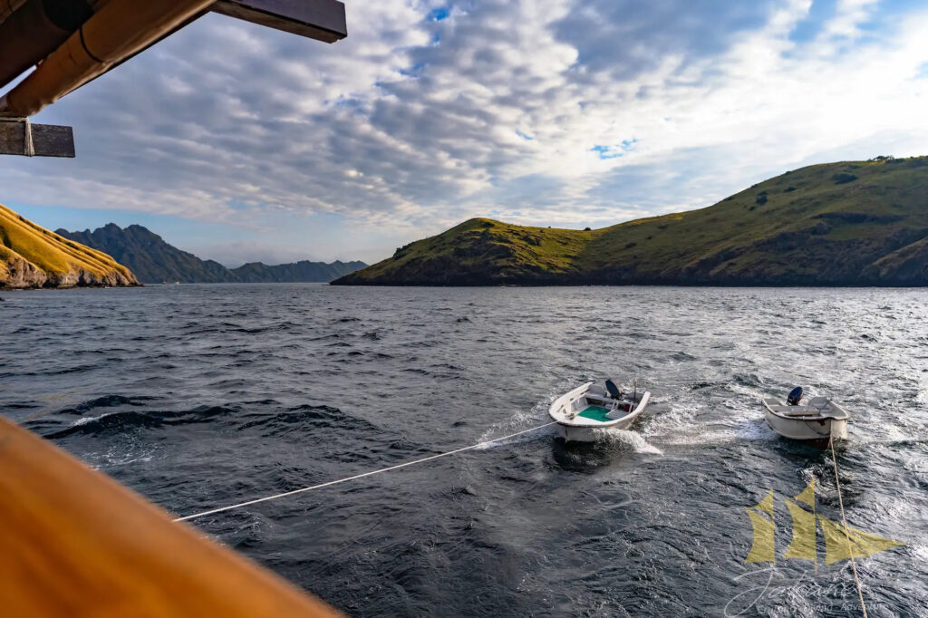 Tender boats towed behind Jakare near green coastal hills