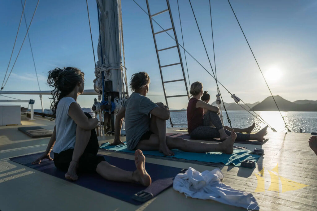 Guests practice yoga on deck facing the water at dusk