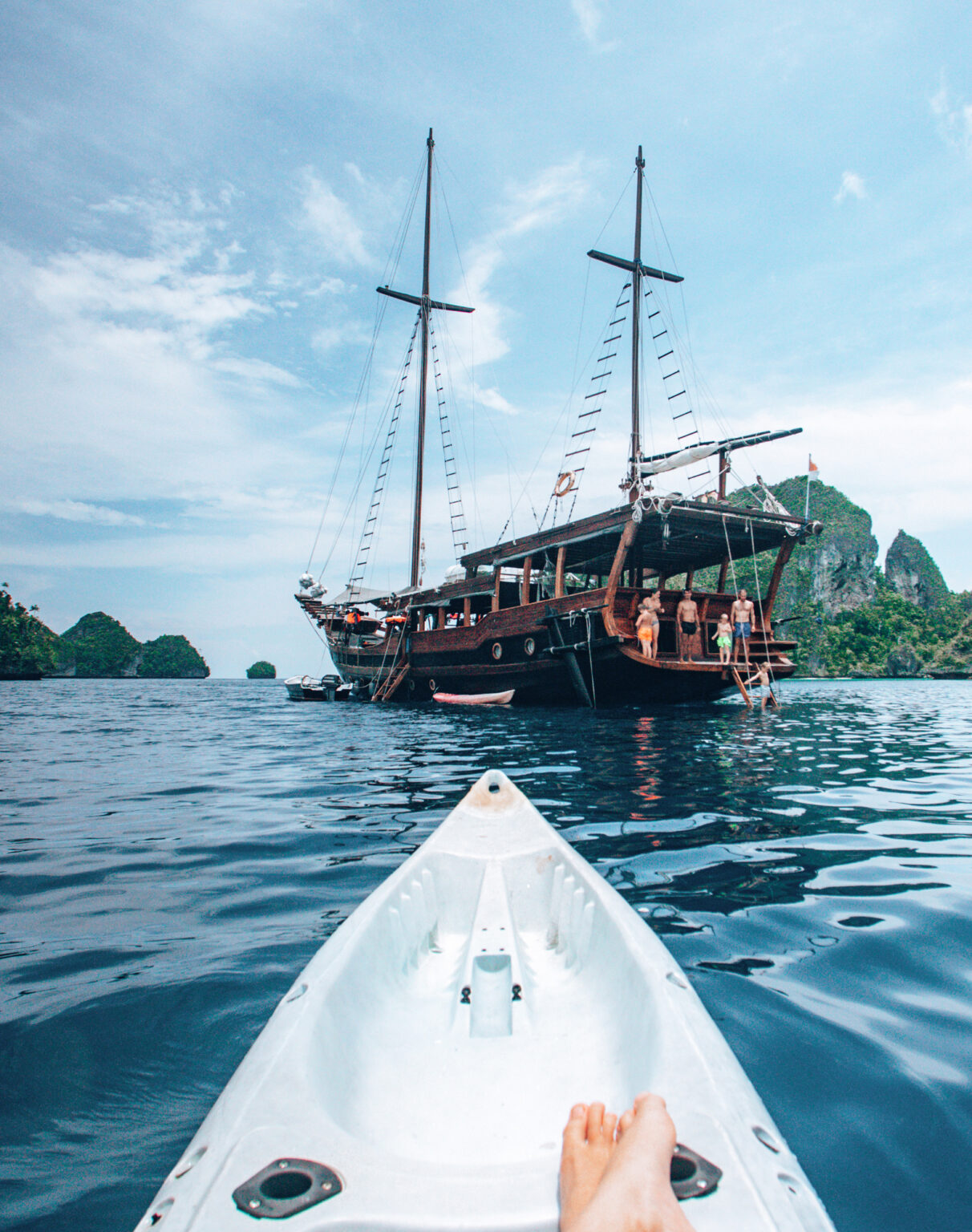 View from a kayak paddling toward a phinisi liveaboard anchored among Komodo islands