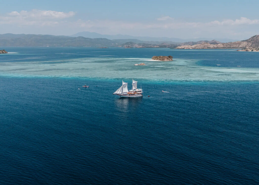 Kayra under sail above a shallow reef, aerial view