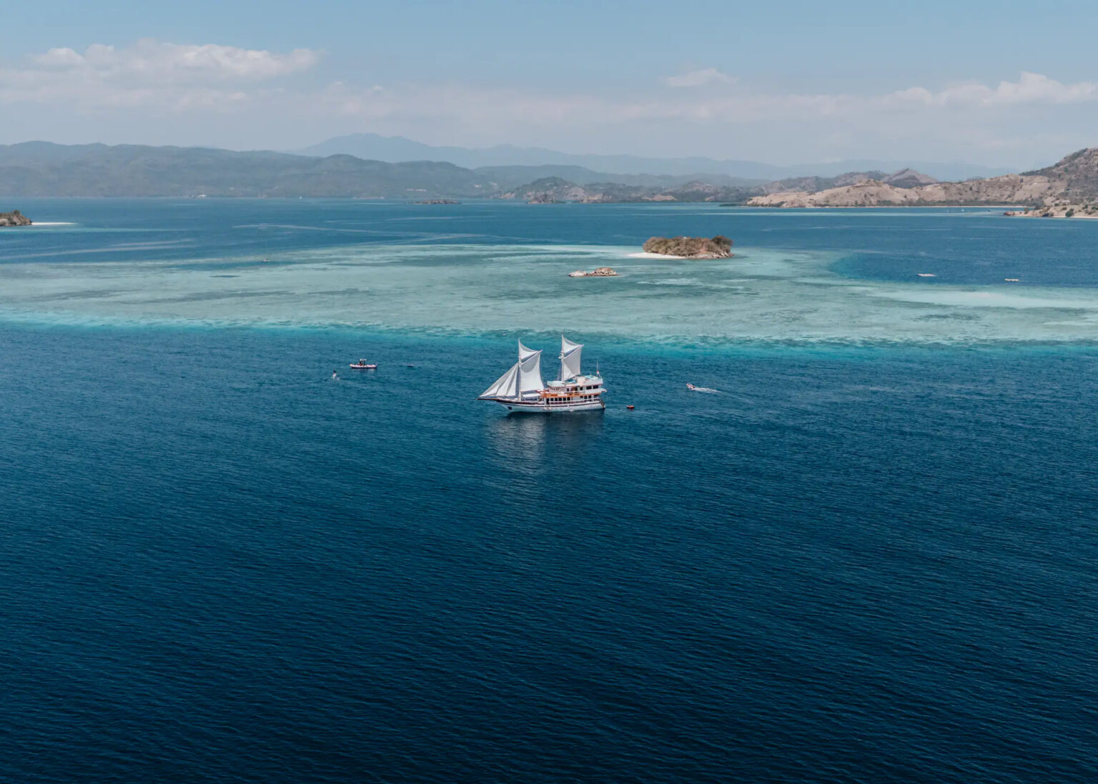 Kayra under sail above a shallow reef, aerial view