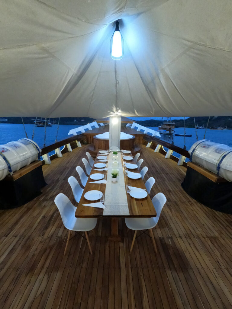 Bow deck dinner table set for a group with the canopy overhead at dusk