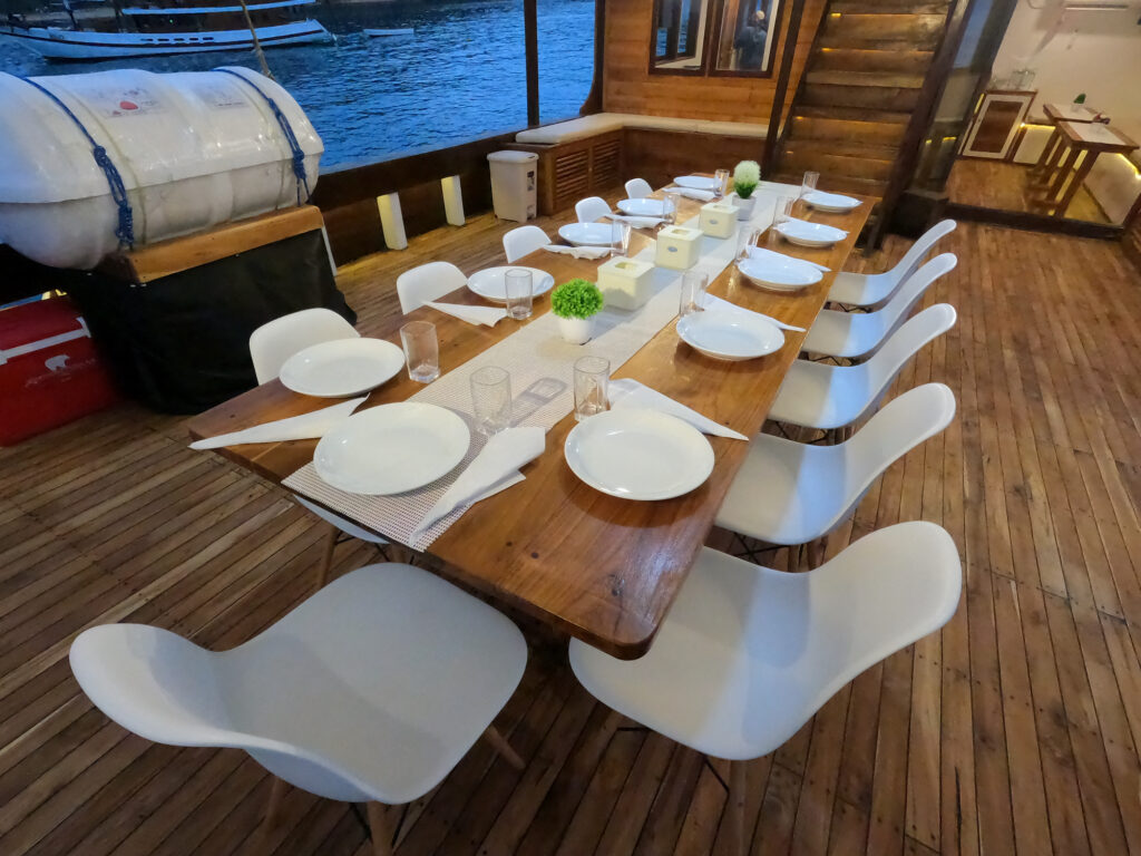 Deck dinner table set with plates and glasses under harbor lights at night