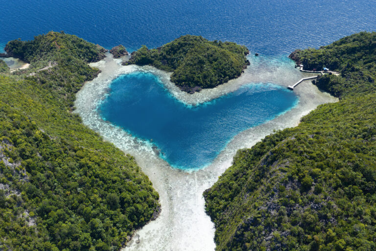 Heart-shaped Love Lagoon ringed by forested karst and white sand seen from above, Raja Ampat