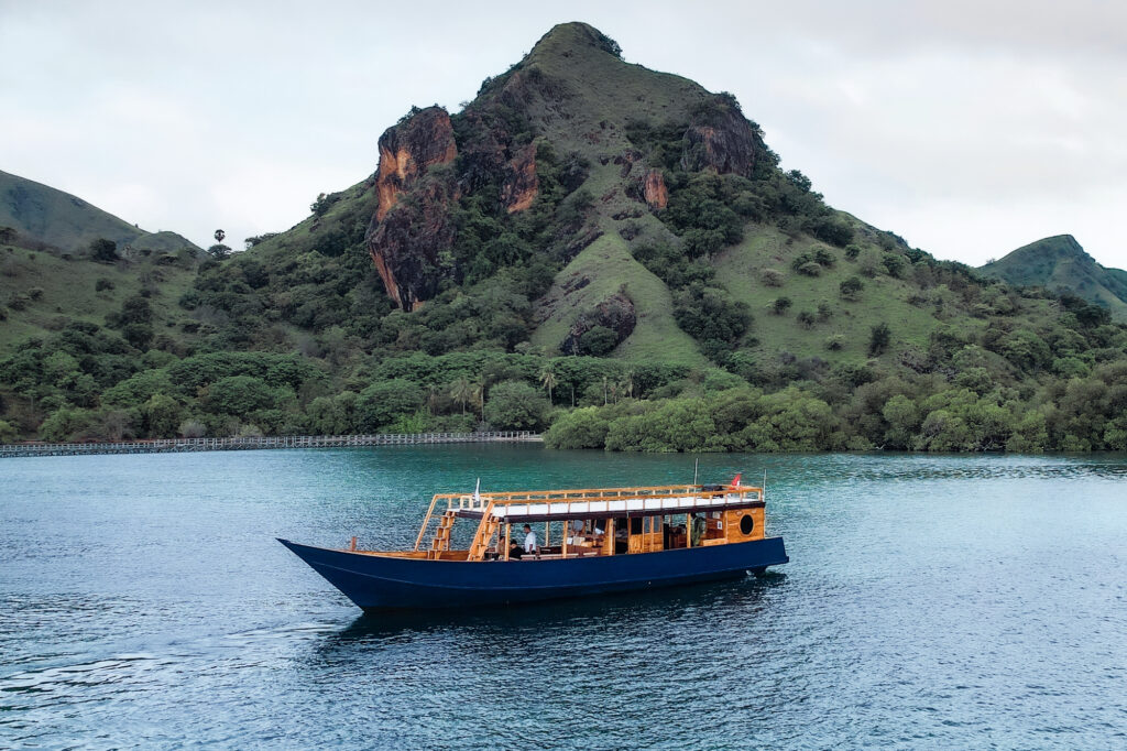 Wooden open-deck vessel with travelers cruising below green hills, Komodo National Park
