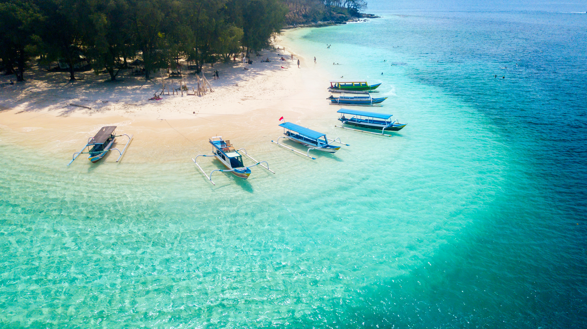 Aerial view of traditional outriggers moored off a white-sand beach in clear turquoise water