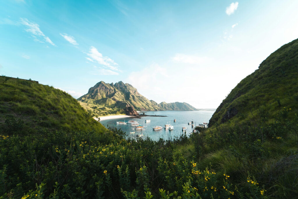 Vessels anchored in a bay below jagged peaks, seen between green hillsides on Padar