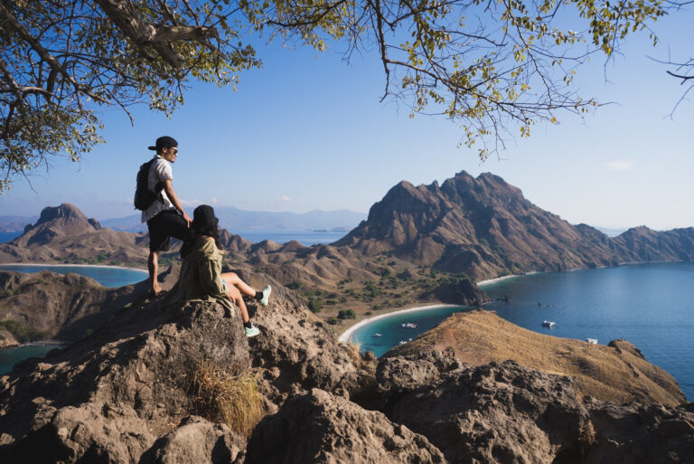Two travelers on the Padar Island ridge above three bays, dry-season light, the best time to visit Komodo Island