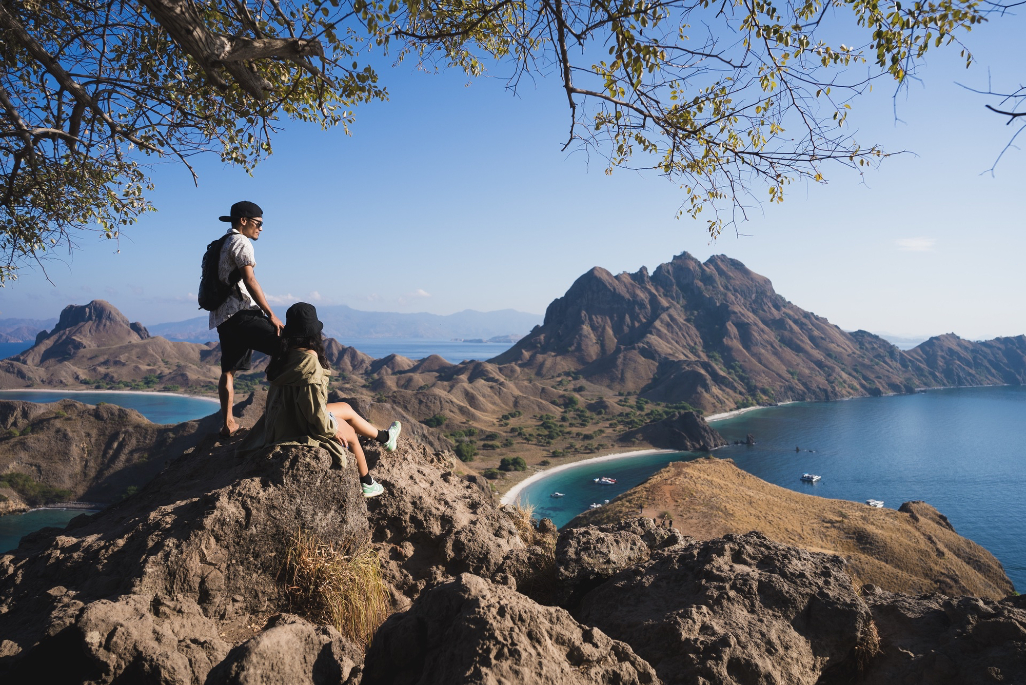 Two travelers on the Padar Island ridge above three bays, dry-season light, the best time to visit Komodo Island