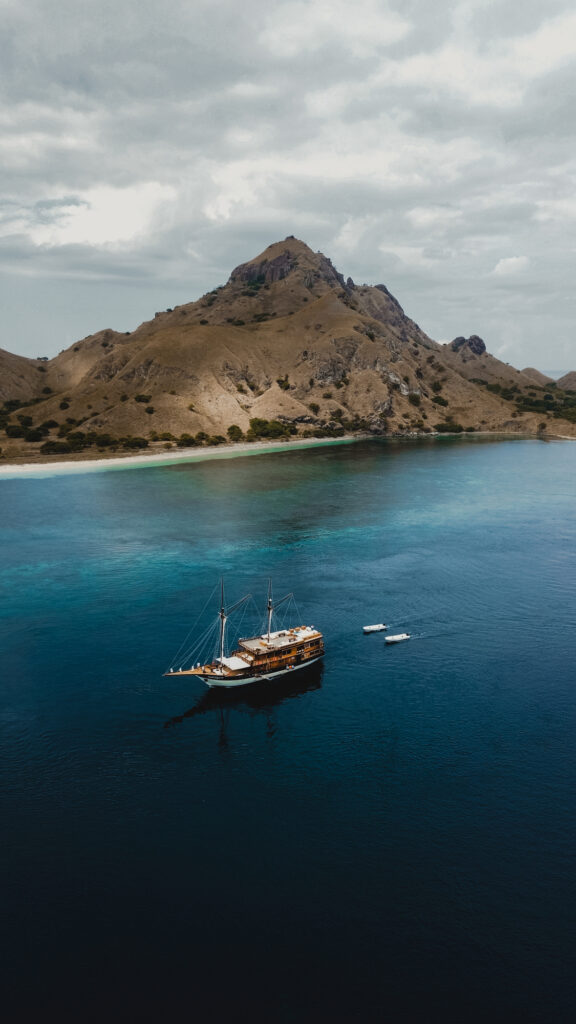 Aerial view of Papiton Allo Komodo liveaboard anchored below a steep island ridge