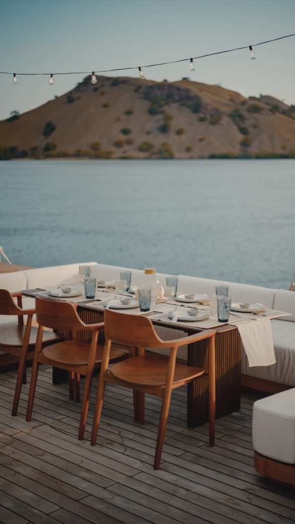 Alfresco dinner table under festoon lights with a bare island hill across the water