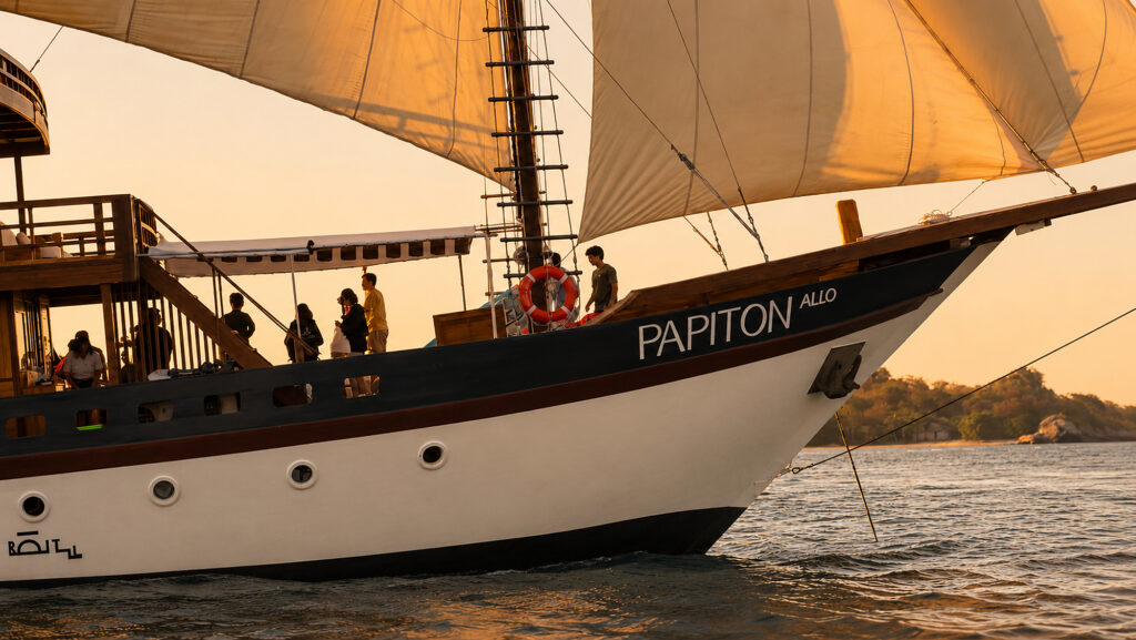 Papiton Allo bow with guests on the foredeck in golden sunset light