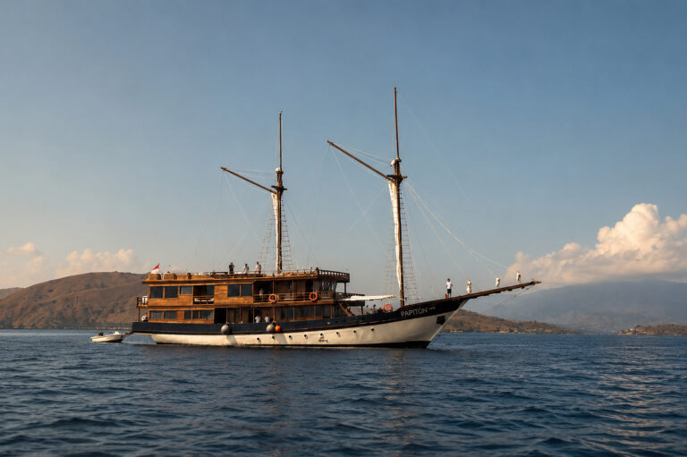 Papiton Allo Komodo liveaboard at anchor with a tender alongside and hills behind