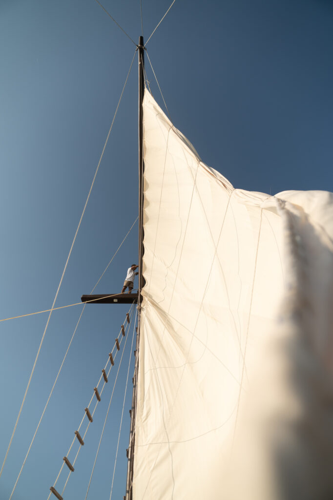 Crew member on the boom below the mainsail against a clear blue sky