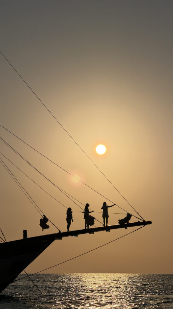 Guests silhouetted along the bowsprit of Papiton Allo against the setting sun