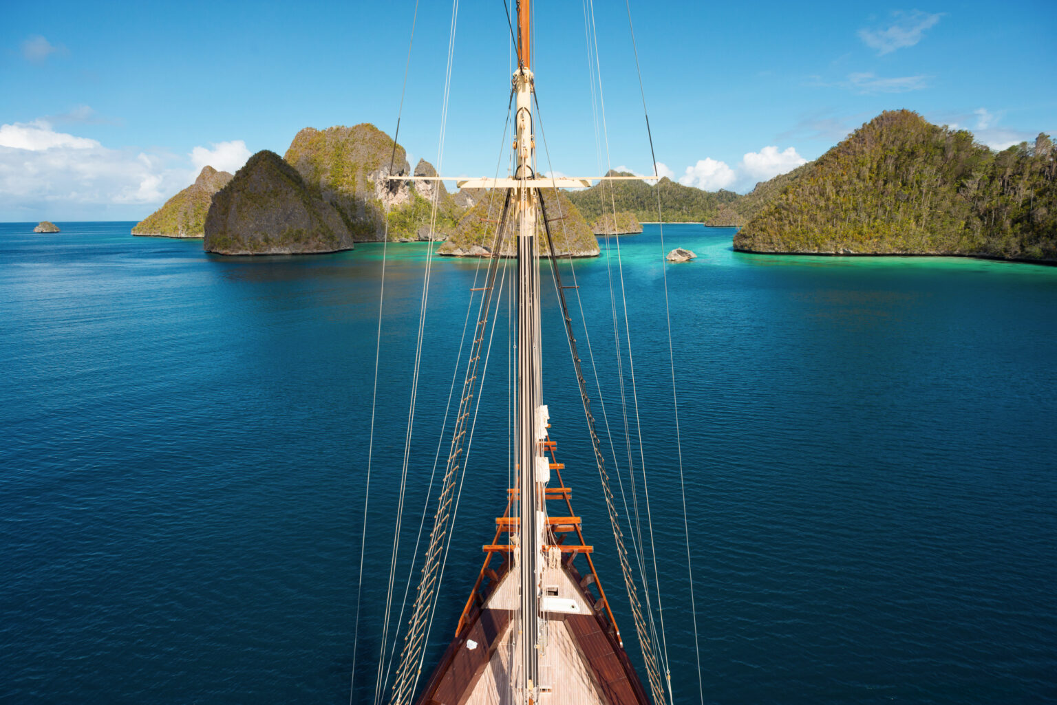 View along a phinisi bowsprit and rigging toward karst islands on calm water, Raja Ampat
