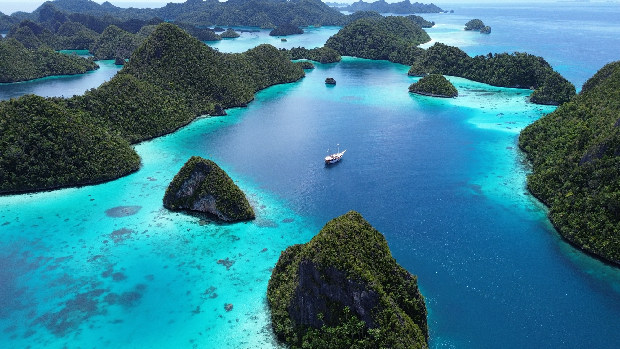 Kelor Island hilltop view over a white sand spit, anchored vessels and golden dry hills