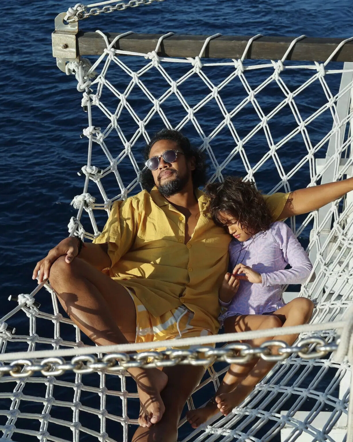 Man and girl relaxing in the bow net of a phinisi over deep blue water