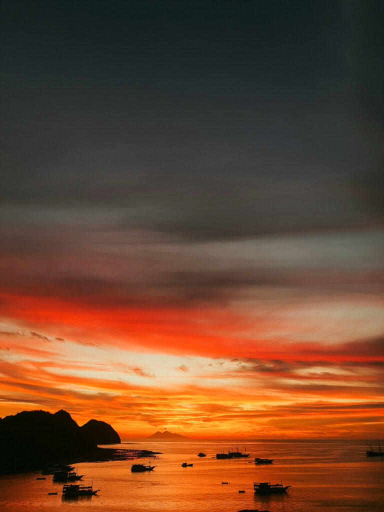 Deep red sunset sky over Labuan Bajo bay with small vessels moored below