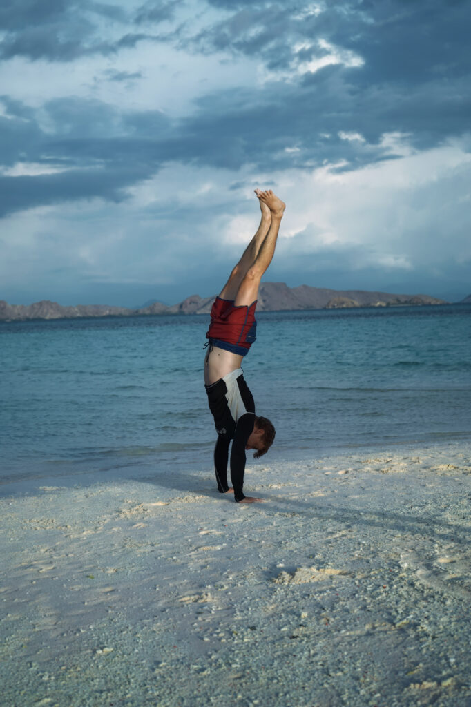 Traveler doing a handstand on a white sandbar under a stormy sky, Komodo National Park