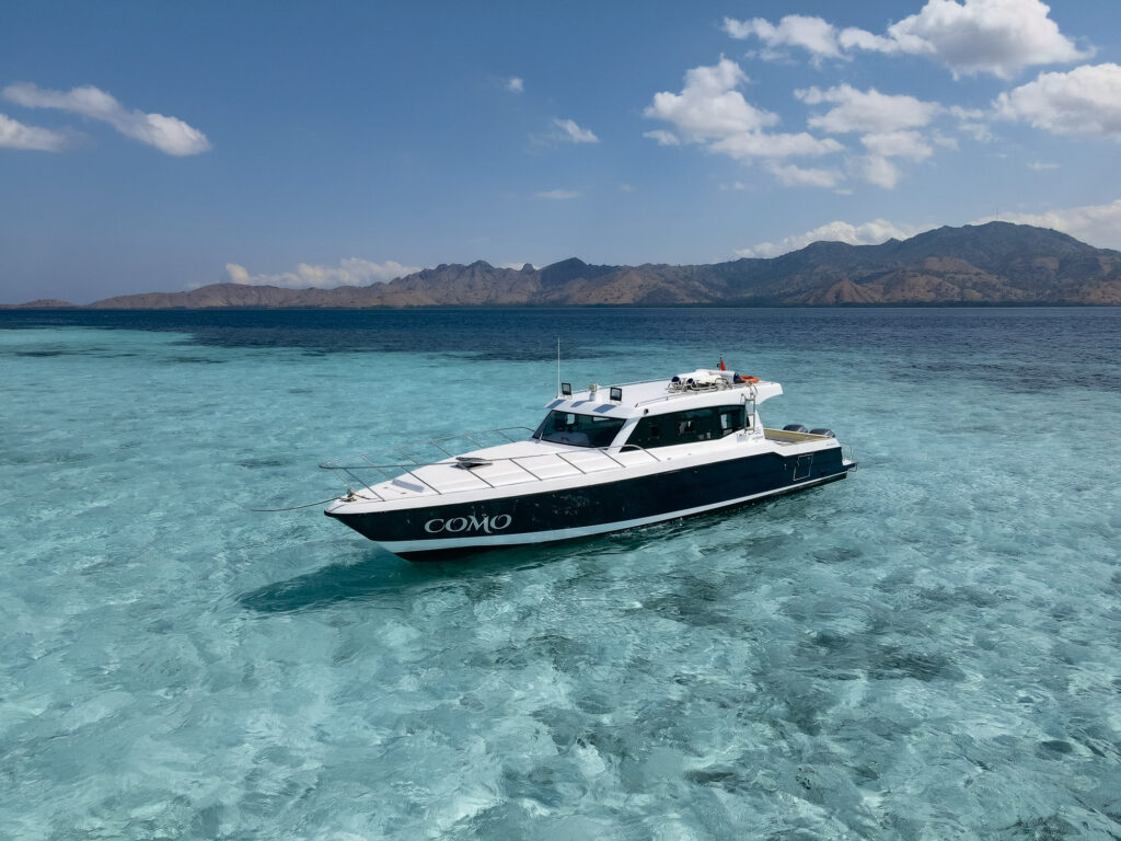 Speedboat idling in shallow turquoise water with dry hills behind, Komodo National Park