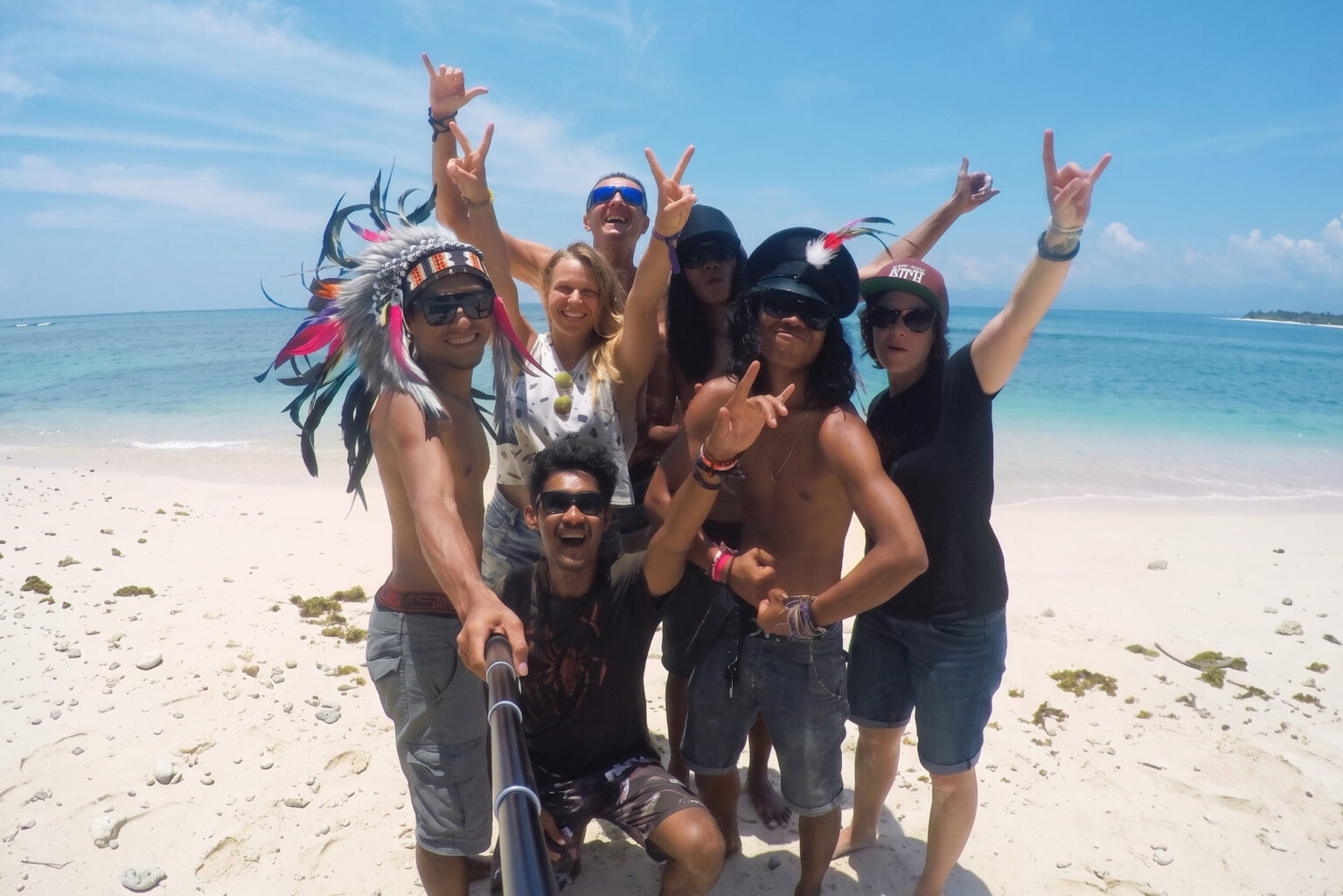Crew and travelers throw peace signs in a group selfie on a white sand beach